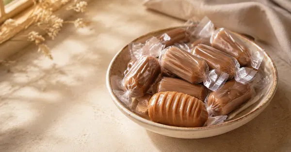 Illustration: a shallow bowl of individually wrapped caramel eclairs with one unwrapped soft caramel sweet Illustration: a shallow bowl of individually wrapped caramel eclairs with one unwrapped soft caramel sweet