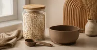 Illustration: fine dry oat flakes in a sealed glass jar beside a clean empty silicone bowl and measuring spoon, no baby