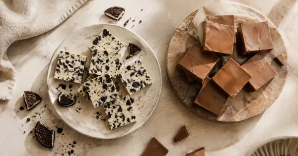 Illustration: white confection squares with dark cookie crumbs beside milk chocolate squares, balanced flat lay Illustration: white confection squares with dark cookie crumbs beside milk chocolate squares, balanced flat lay