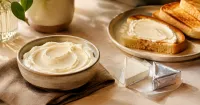 Illustration: unbranded cream cheese in a ceramic bowl and foil-wrapped cheese triangles beside toast on a breakfast table