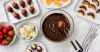 Clean, dried strawberries, banana and orange pieces being dipped in dark chocolate