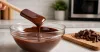 Dry glass bowl of smoothly melted chocolate with spatula and chopped pieces