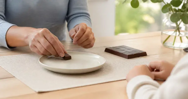 Parent portioning a small chocolate piece on a child-safe plate at a seated table Parent portioning a small chocolate piece on a child-safe plate at a seated table